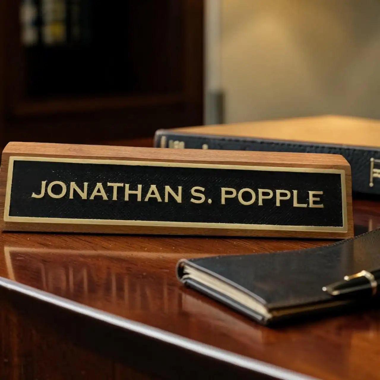 Nameplate with 'Jonathan S. Popple' on a wooden surface with a pen and notebook.