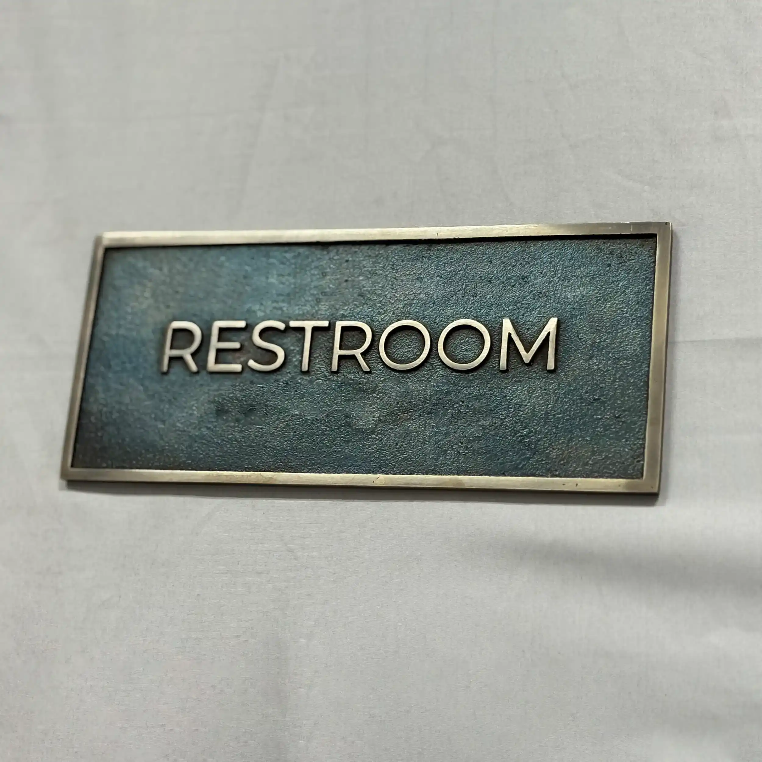 Rectangular sign with 'RESTROOM' text on a textured surface