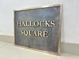 Metal sign with 'HALLOCKS SQUARE' text on a plain background