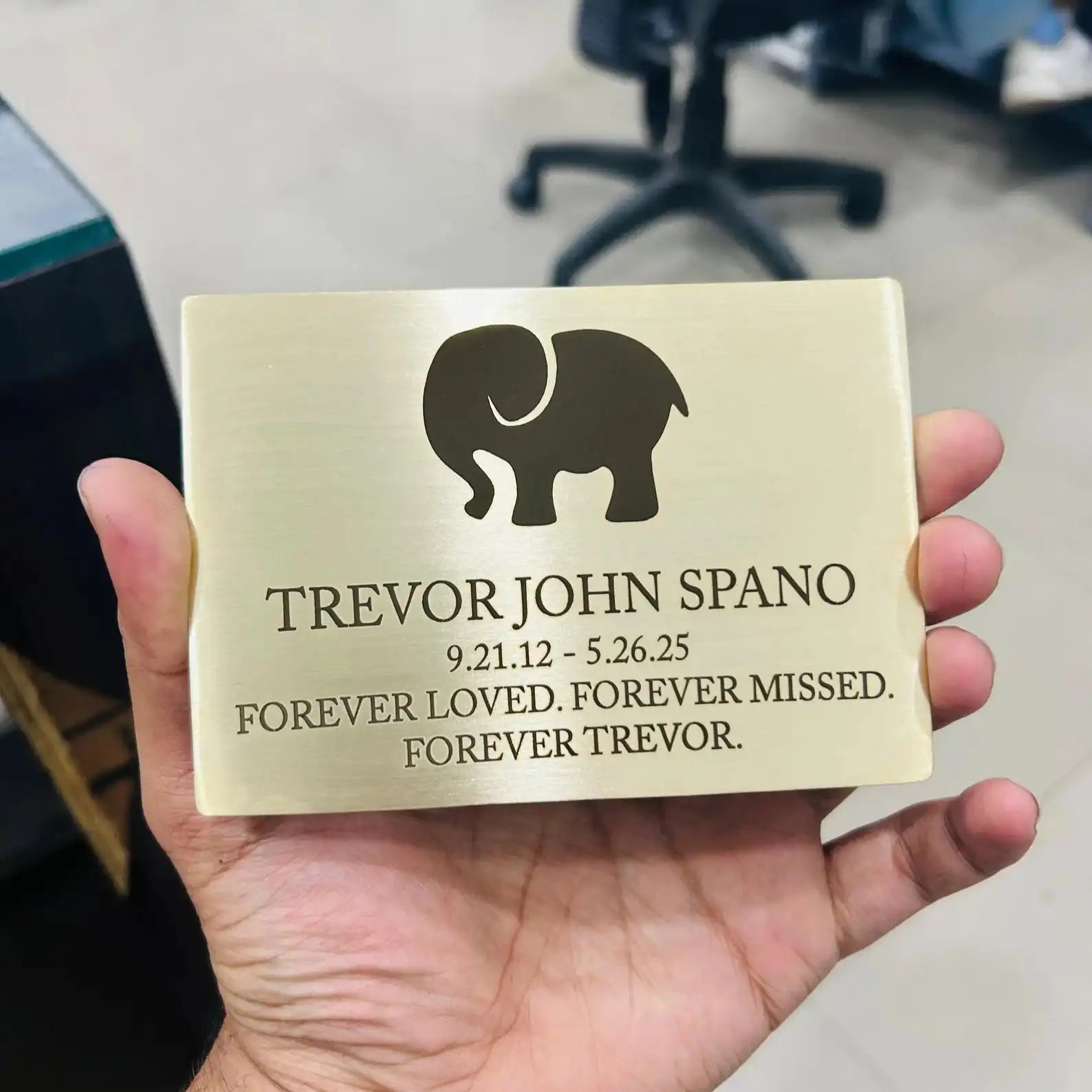 Brass Memorial plaque with elephant silhouette and text held in a hand, blurred office background