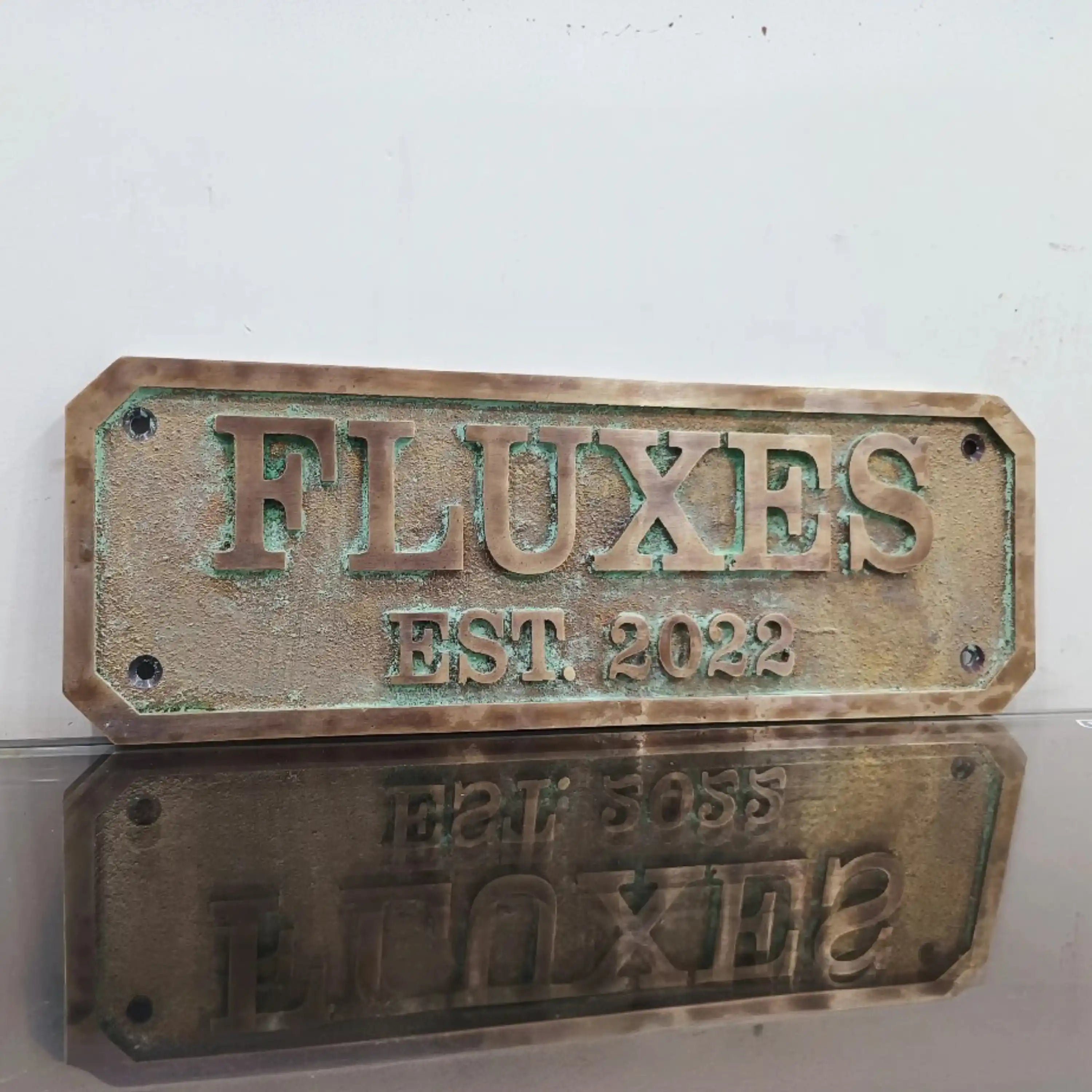 Bronze plaque with 'FLUXES EST. 2022' text on a white background