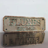 Bronze plaque with 'FLUXES EST. 2022' text on a white background