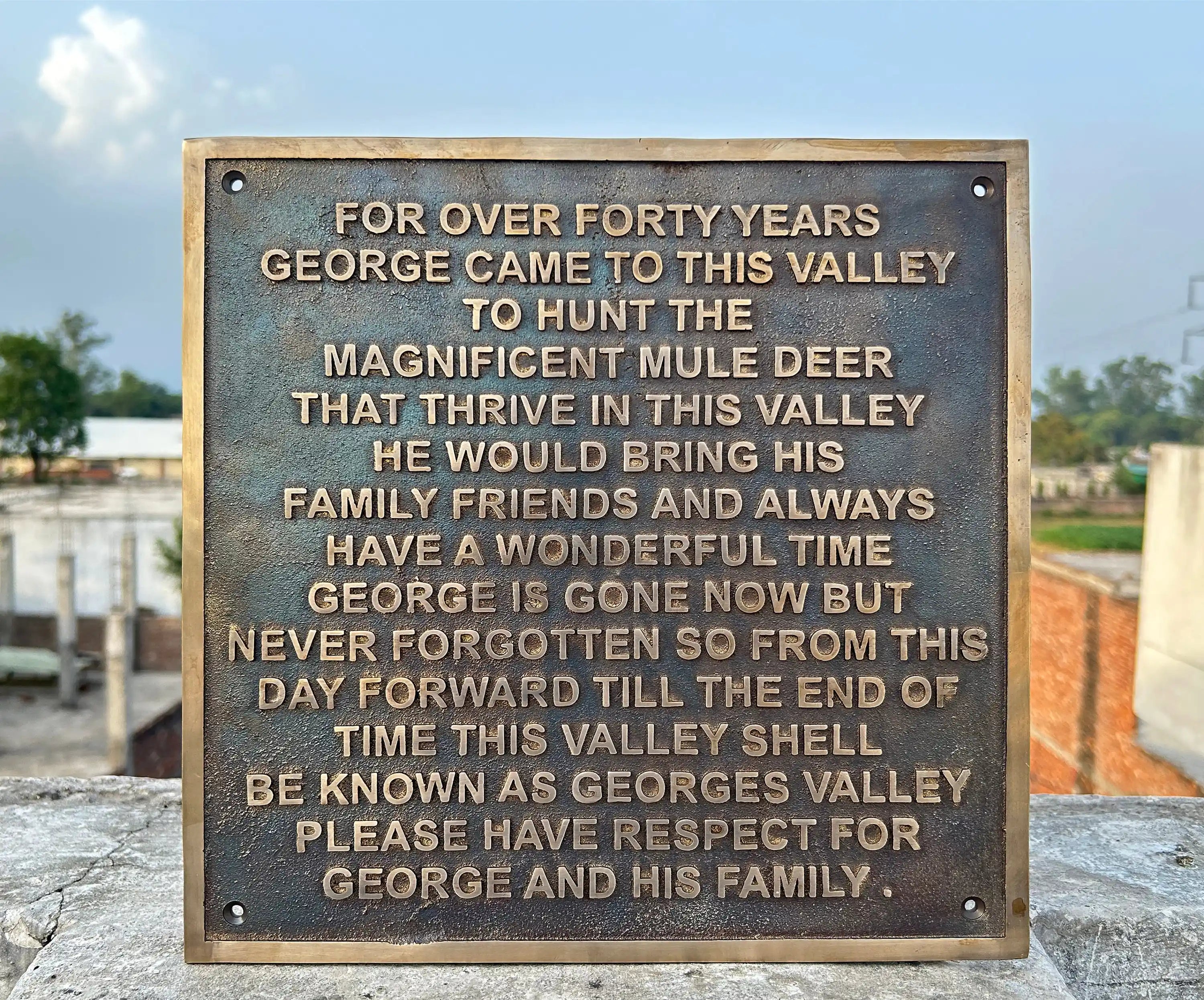 Bronze plaque with engraved text on a stone ledge outdoors