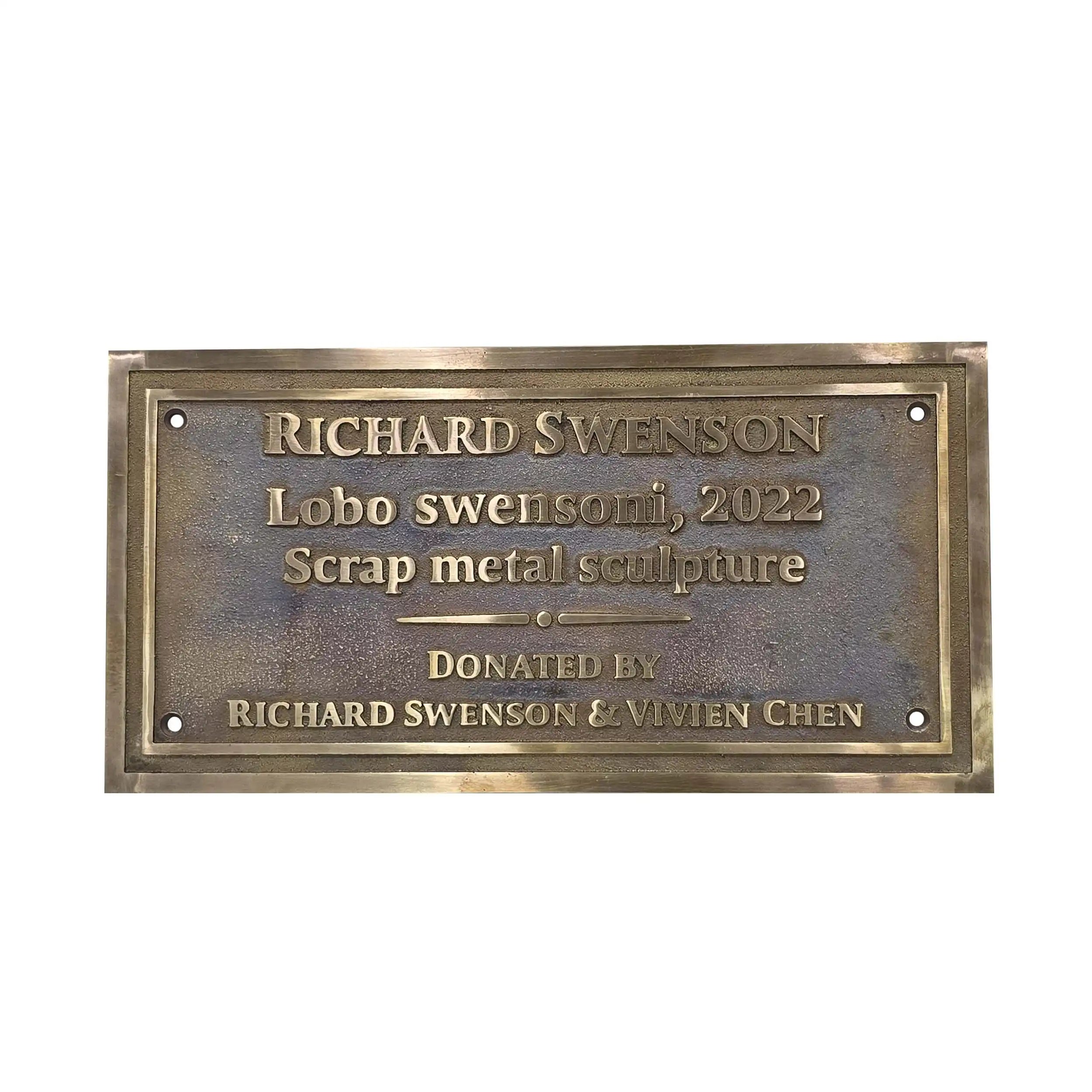 A rectangular bronze metal plaque with engraved text reading 'RICHARD SWENSON Lobo swenson, 2022 Scrap metal sculpture DONATED BY RICHARD SWENSON & VIVIEN CHEN' on a plain white background.