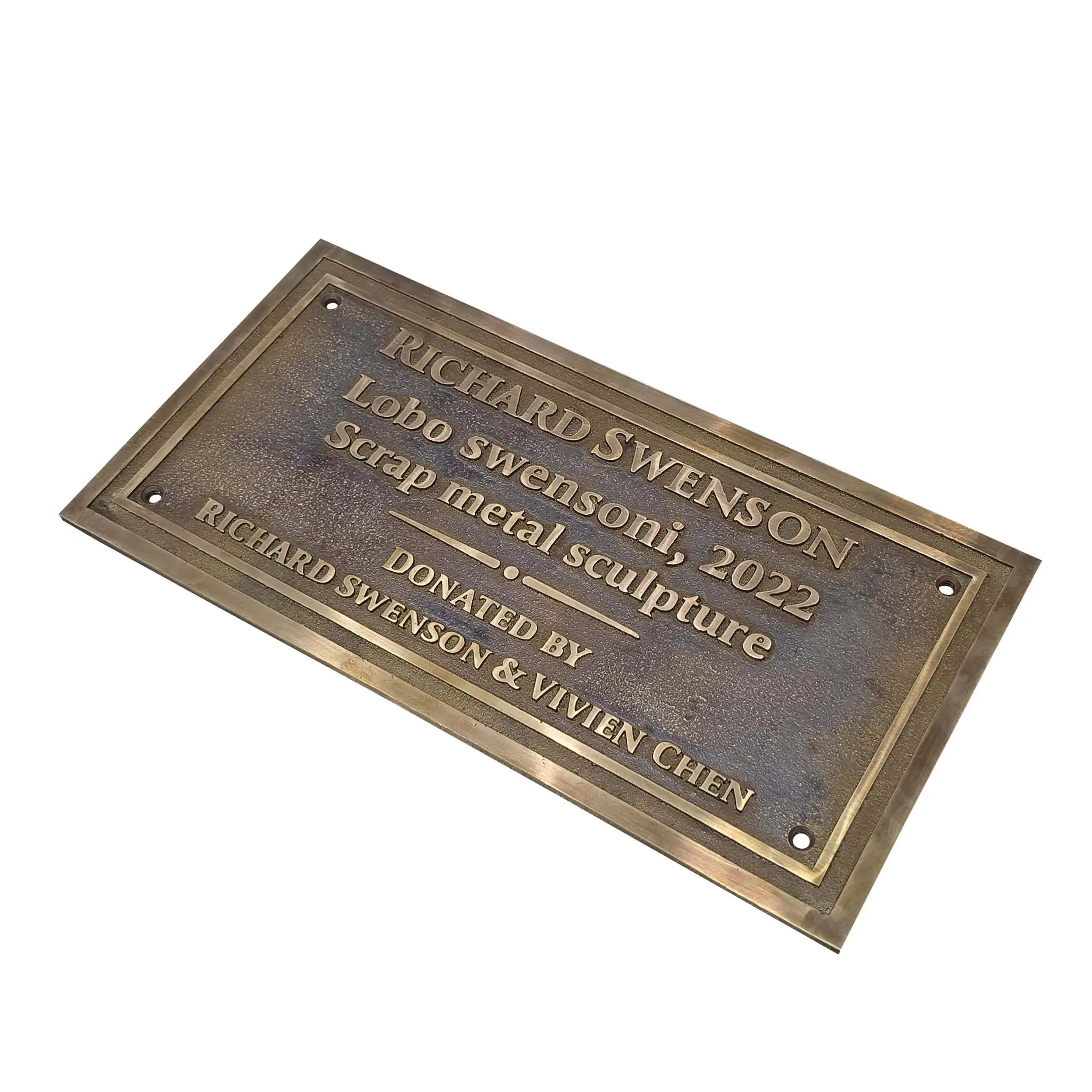 A rectangular bronze metal plaque with engraved text, shown at an angle on a plain white background. The plaque reads: 'RICHARD SWENSON Lobo swenson, 2022 Scrap metal sculpture DONATED BY RICHARD SWENSON & VIVIEN CHEN'.