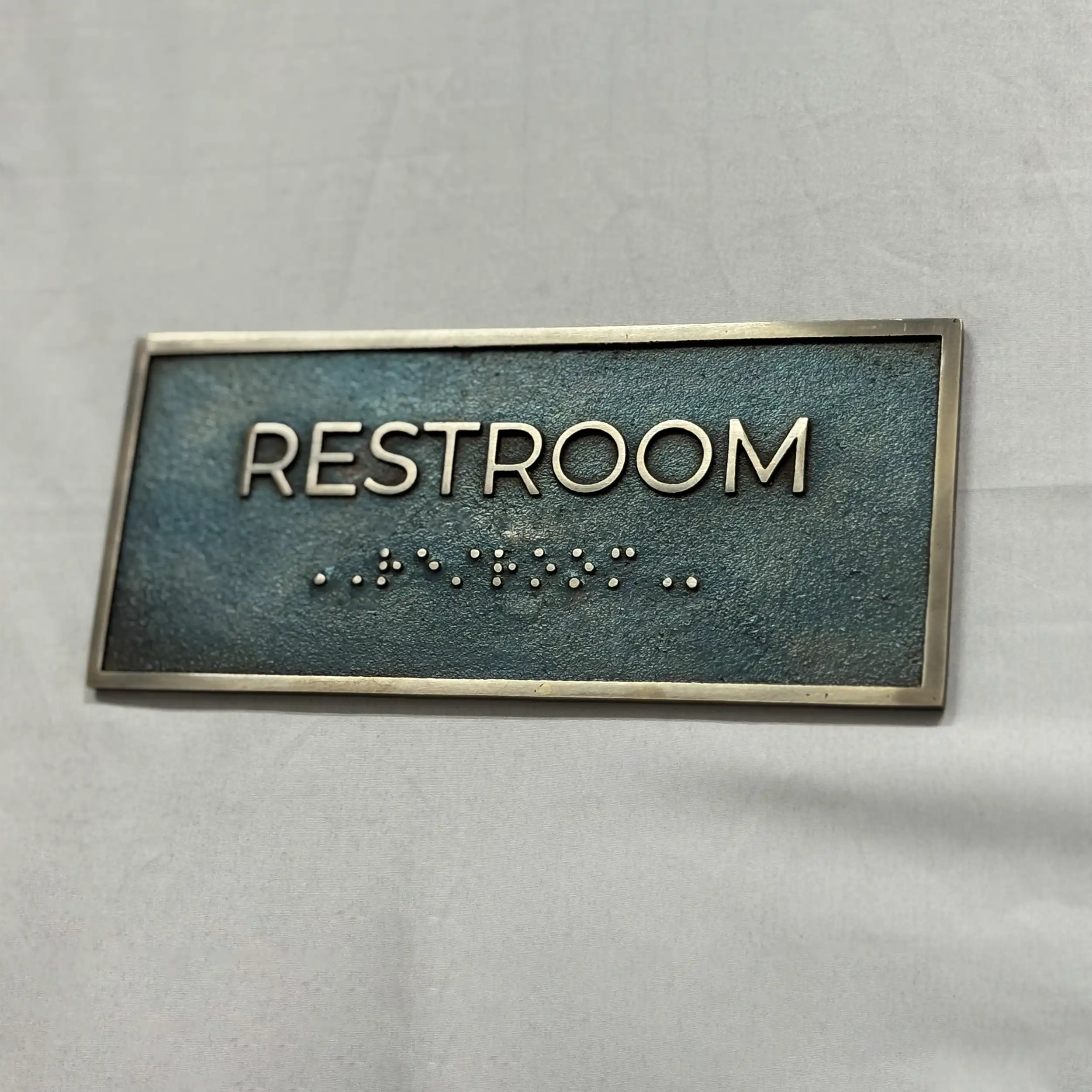 Rectangular sign with 'RESTROOM' text and braille on a gray background