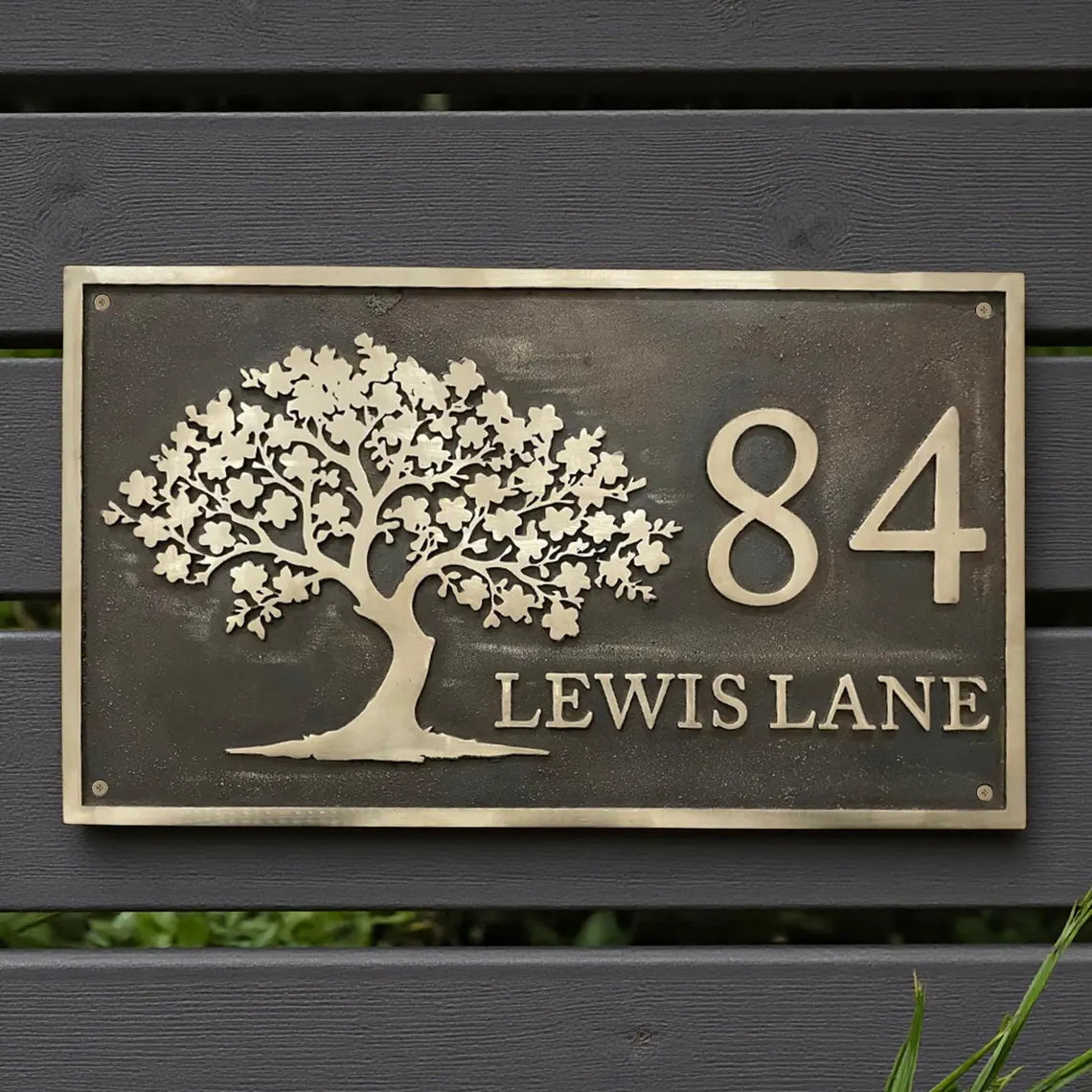 Bronze house number sign with tree design on a wooden background