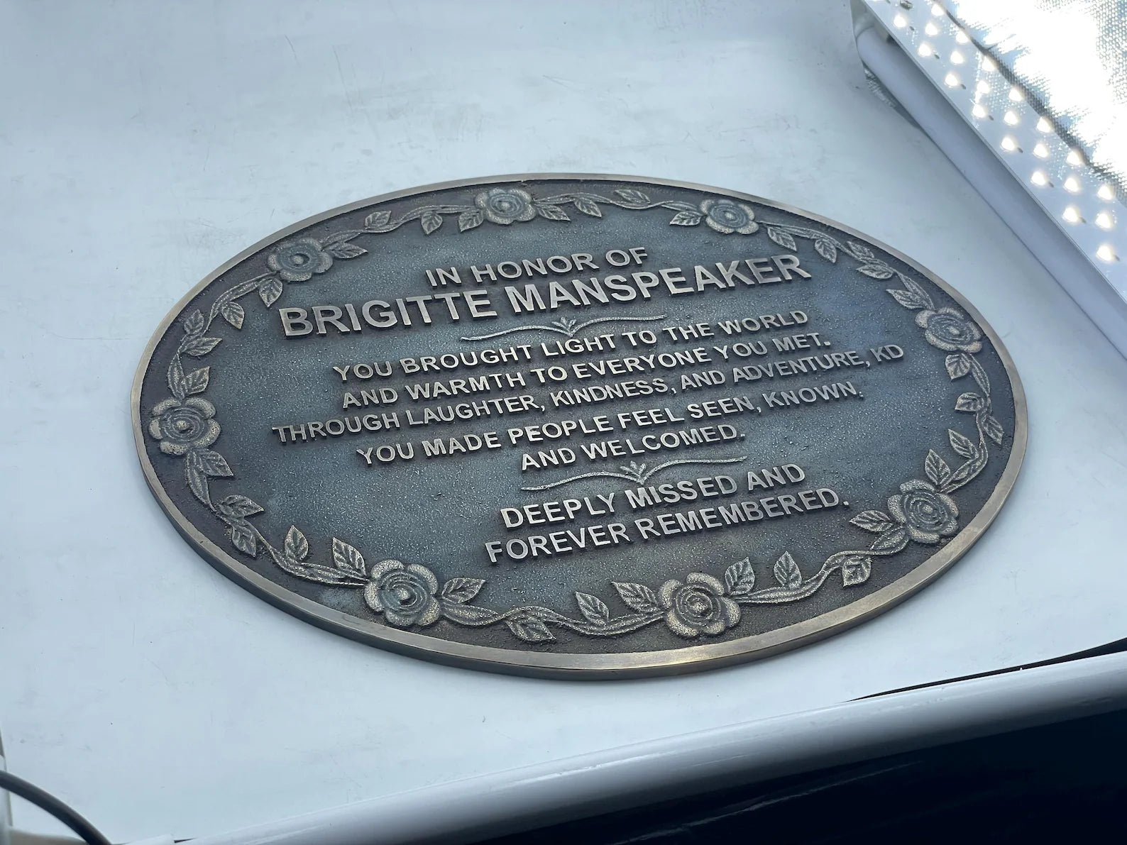 Memorial plaque on a car window honoring Brigitte Manspeaker with engraved text.