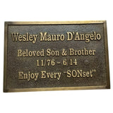 A rectangular bronze memorial plaque with raised lettering that reads 'Wesley Mauro D'Angelo, Beloved Son & Brother, 11/76 - 6/14, Enjoy Every "SONset"' on a plain white background.