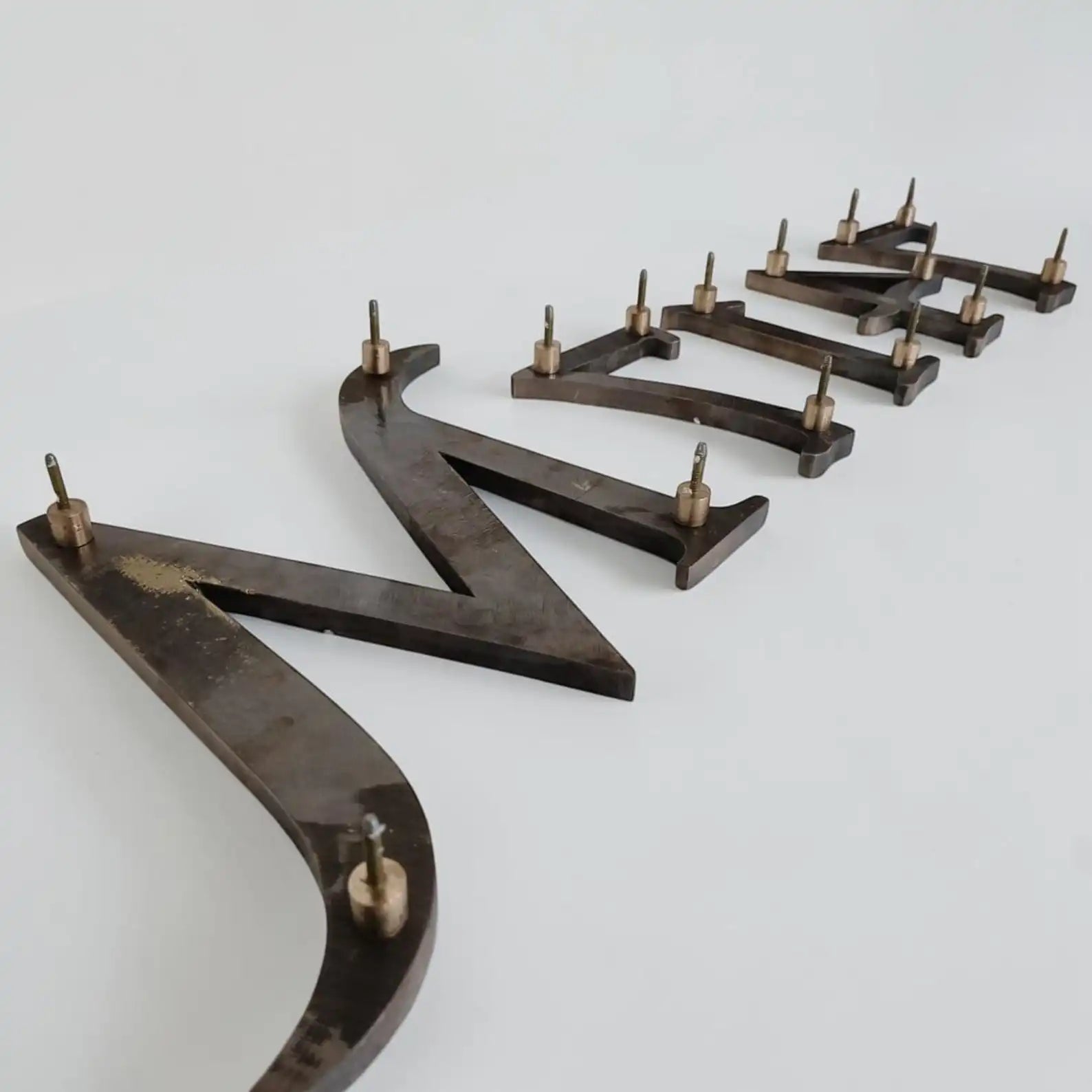 A set of dark metal letters, arranged in a row on a plain light background.