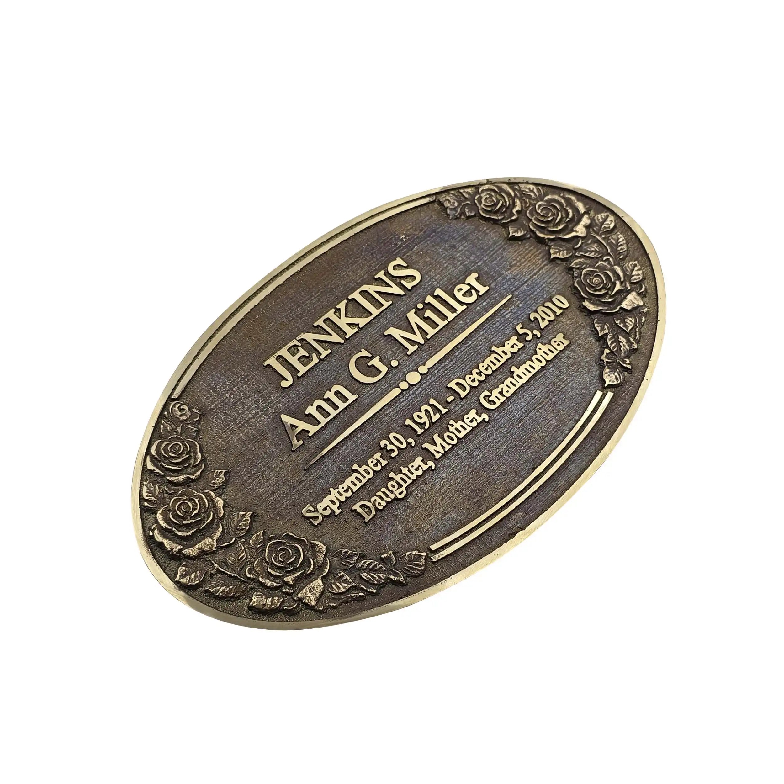 An oval bronze-colored metal memorial plaque engraved with the name 'JENKINS Ann G. Miller' and a date, decorated with embossed roses around the border, shown on a plain white background.