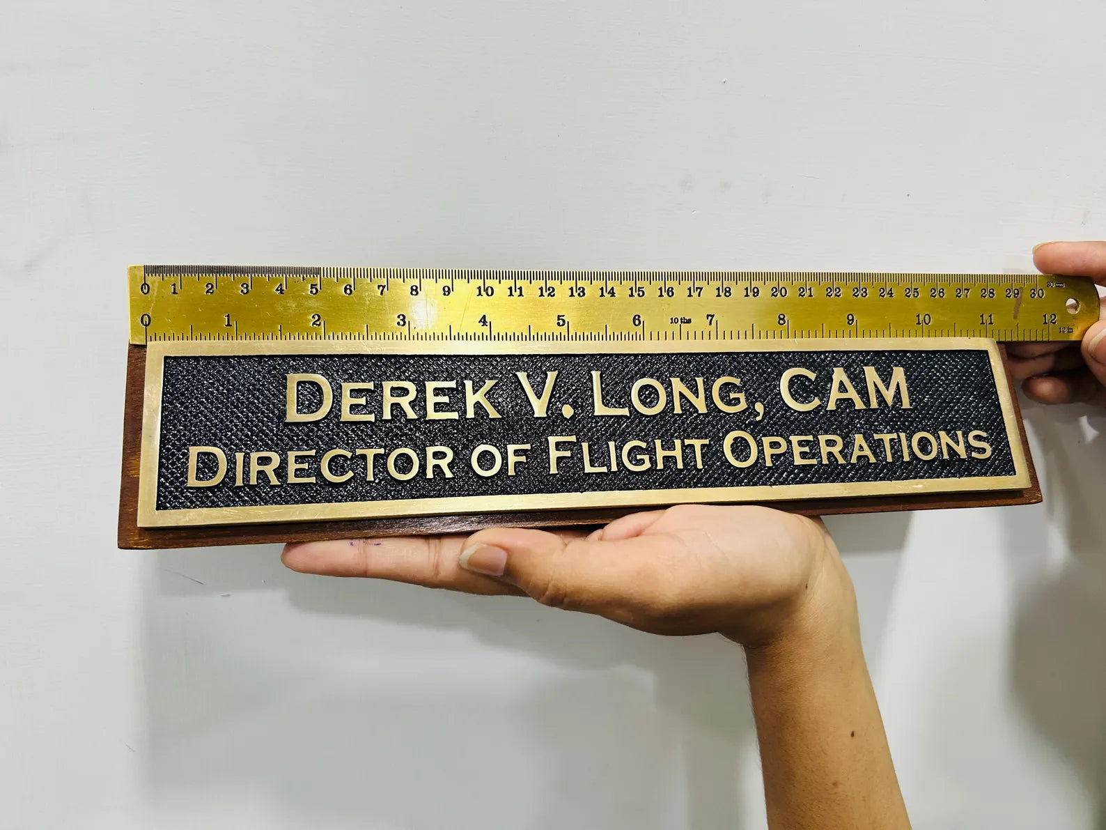 Nameplate with engraved text held by a hand against a white background