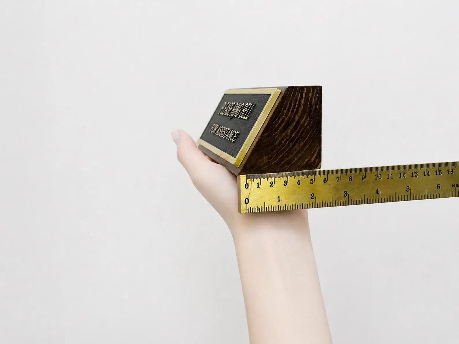 Hand holding a gold bar with a ruler for scale on a light gray background