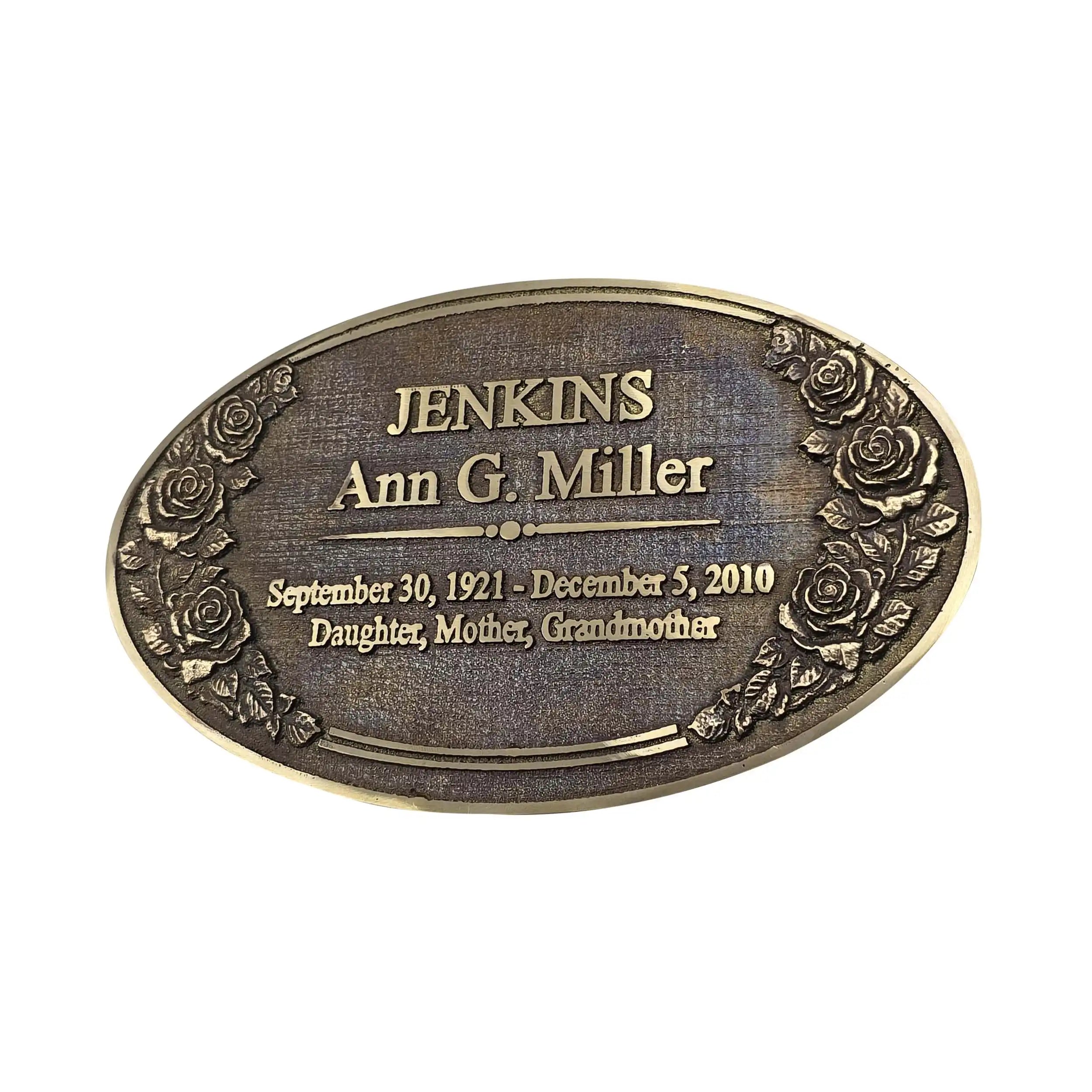An oval bronze-colored metal memorial plaque with engraved text reading 'JENKINS Ann G. Miller' and dates and relationship details, decorated with embossed roses around the border, shown on a plain white background.
